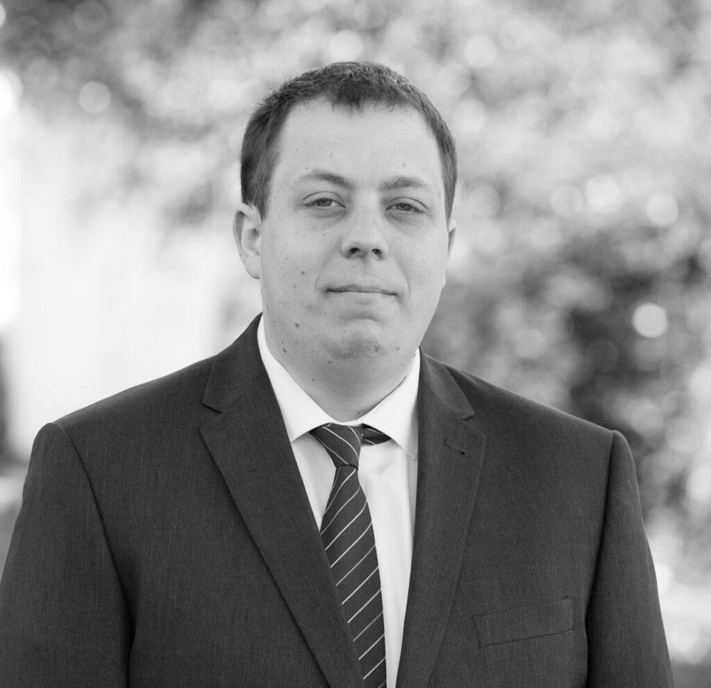 Black and white photo of man looking into camera dressed in suit. Purple background with Insphere logo